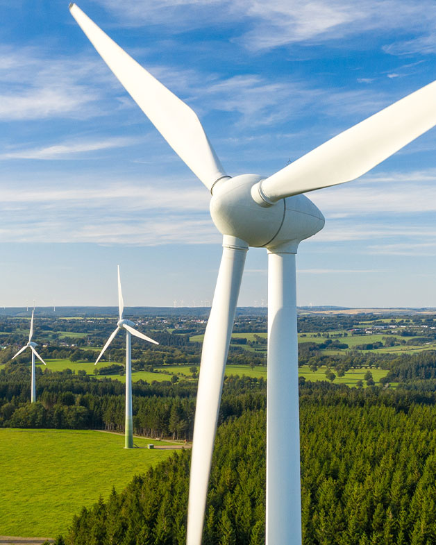 Image of wind blade against blue sky and green fields.