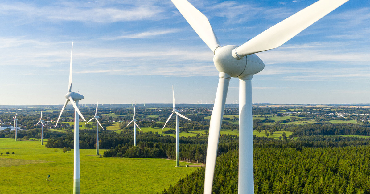 Image of wind blade against blue sky and green fields.